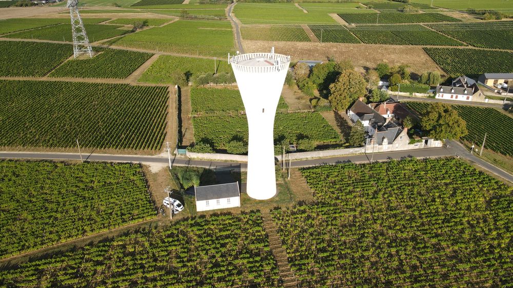 Luftaufnahme eines weißen Wasserturms zwischen Weinbergen, von schräg oben fotografiert